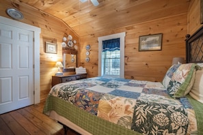 A wooden cabin bedroom with a bed, a window with blinds, a door, and wall-mounted plates. - Georgia Bell's| Vintage Farmhouse by Chattahoochee (Helen)