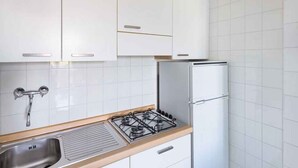 A kitchen with white cabinets, a stainless steel sink, a gas stove, and a white refrigerator. - Holiday apartment with air conditioning and balcony (Lignano)