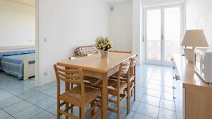 A compact room with a dining table, chairs, a bed, and a kitchenette. - Holiday apartment with air conditioning and balcony (Lignano)