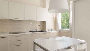 A modern kitchen with white cabinets, a sink, and a window providing natural light. - Holiday apartment mit Klimaanlage und Balkon (Lignano)