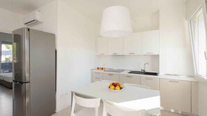 A modern kitchen with white cabinets, a stainless steel refrigerator, and a white dining table with chairs. - Holiday apartment mit Klimaanlage und Balkon (Lignano)