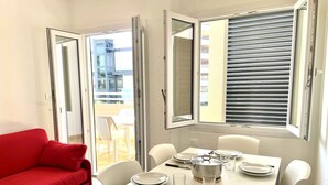Un coin repas avec une table dressée pour quatre personnes, des chaises blanches, un canapé rouge et une vue à travers la porte coulissante ouverte.