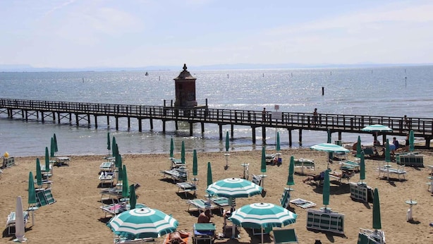 Une plage bordée de rangées de parasols et de chaises longues, une jetée s’avançant dans l’eau et une petite structure en forme de tour.