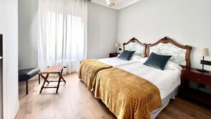Une chambre à coucher avec un grand lit, deux tables de chevet, une chaise et une fenêtre ornée de rideaux légers.