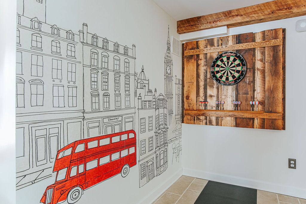 A room with a wall mural of a cityscape, a dartboard, and a red double-decker bus.