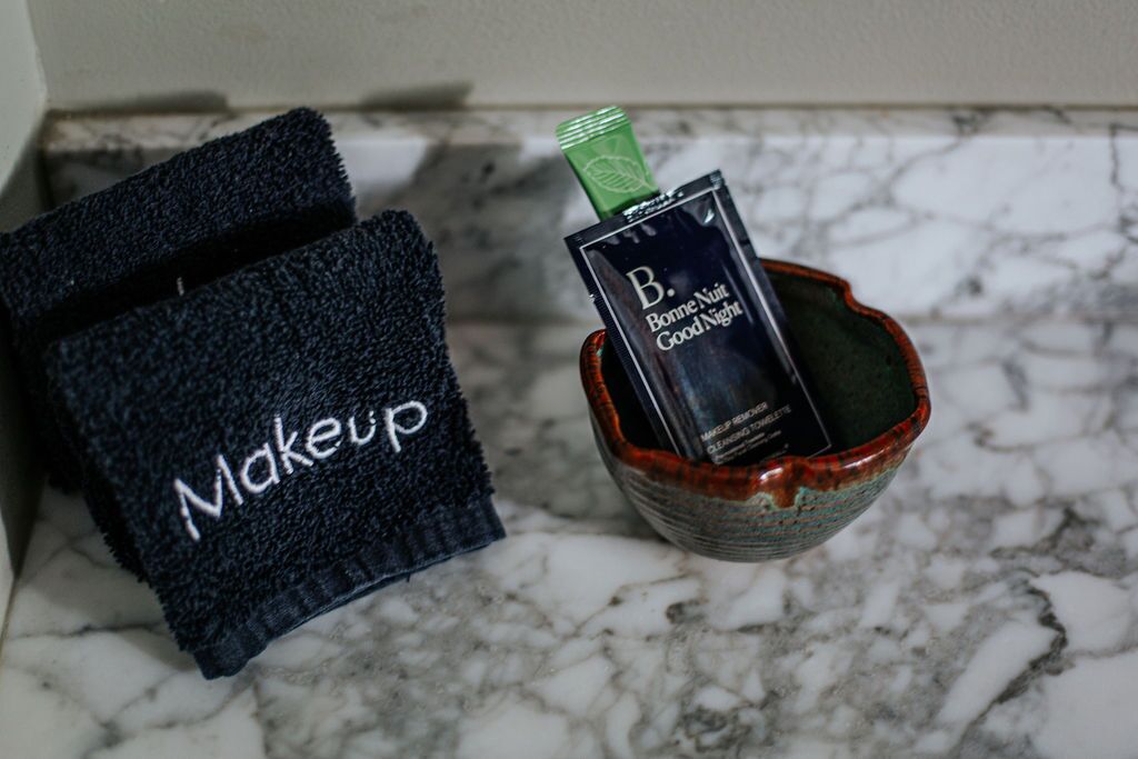 A dark blue towel with "Makeup" written on it, a small ceramic bowl with a makeup product, and a green cap.