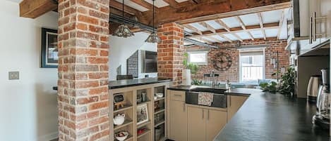 Une cuisine avec des murs en briques apparentes, des poutres en bois et un plan de travail noir.