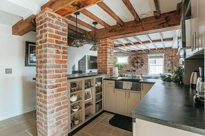 Een keuken met zichtbare bakstenen muren, houten balken en een zwart aanrecht.