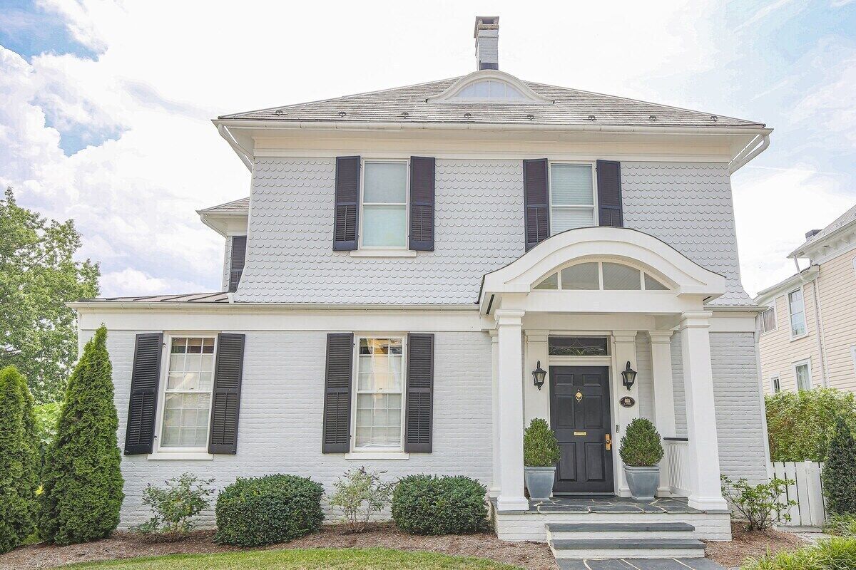 A two-story house with a symmetrical facade, a central entrance with a black door, and a small porch with steps.