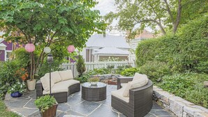 An outdoor patio with wicker furniture, stone flooring, and potted plants.
