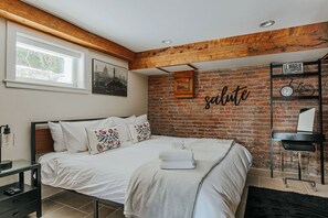 Ein Schlafzimmer mit Backsteinwand, einem Bett mit weißer Bettwäsche, einer Holzbalkendecke und einem Regal mit einem Fahrrad und einem Schild.
