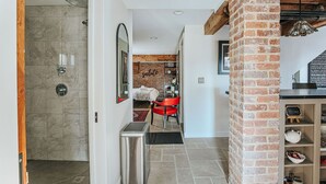 A hotel corridor with a shower, a red chair, a brick column, and a welcome sign.