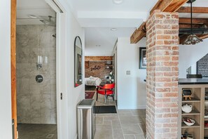 A hotel corridor with a shower, a red chair, a brick column, and a welcome sign.