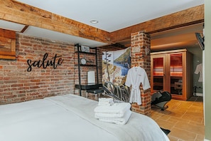 Una habitación de hotel con pared de ladrillo, cama con ropa blanca, perchero, bicicleta y un letrero que dice "salute".