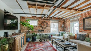A cozy living room with exposed wooden beams, a brick wall, and a large red rug. - The Hideaway Suite: Sauna & Lux Amenities (Staunton)