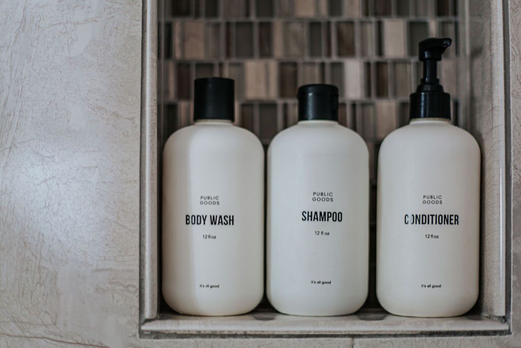 Drie flessen douchegel, shampoo en conditioner in een houten kast.