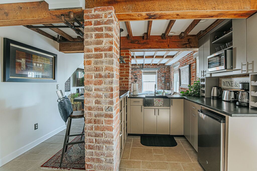 A modern kitchen with exposed brick walls, stainless steel appliances, and a wooden ceiling.