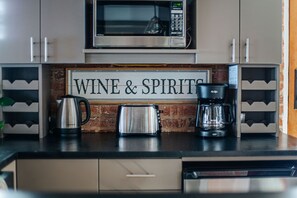Eine Küche mit Mikrowelle aus Edelstahl, Toaster, Kaffeemaschine und einem Schild mit der Aufschrift 'WINE & SPIRITS'.
