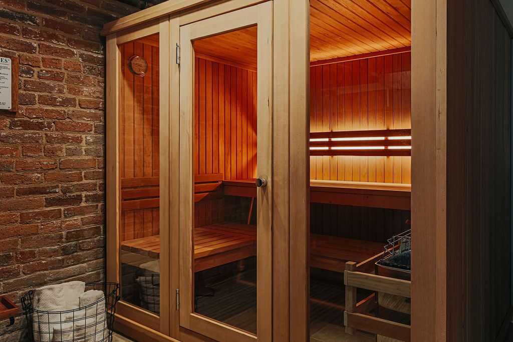 A sauna with wooden benches and glass doors, a brick wall, and a towel rack.