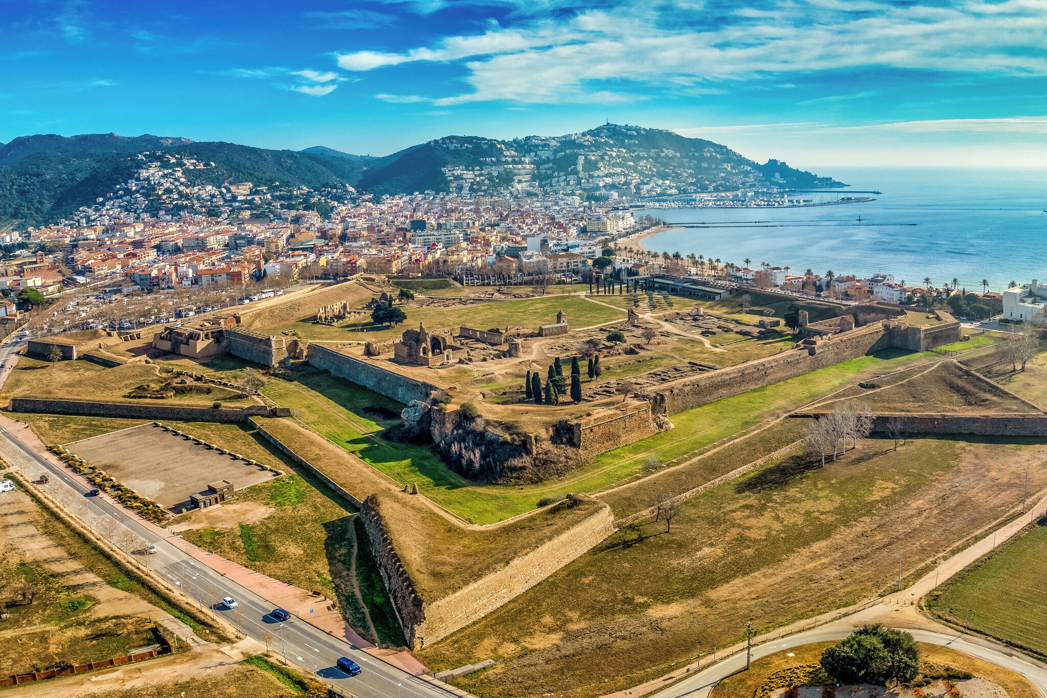 Vue aérienne d’une ville côtière, avec un fort historique, des bâtiments modernes et une vue dégagée sur la mer.