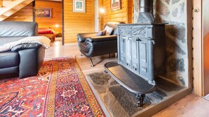 L’intérieur chaleureux d’un chalet en bois comprend un canapé en cuir noir, un tapis coloré, une cheminée en pierre et un escalier en bois.