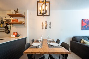 A dining area with a wooden table set for four, chairs, and a pendant light fixture above.