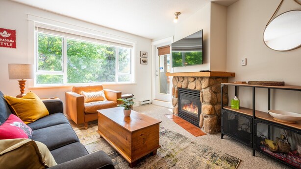 A living room with a stone fireplace, a sofa, a coffee table, and a television mounted above the fireplace.