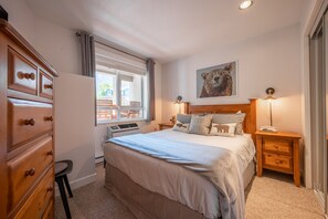 Ein Schlafzimmer mit Bett, einem Holzschrank, Fenster, Heizkörper und einem Bild an der Wand.