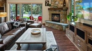 A cozy living room with a stone fireplace, leather furniture, and a large window overlooking a lake. - Luxury Family Waterfront Home | Dock + SUP/Kayak (Sagle)
