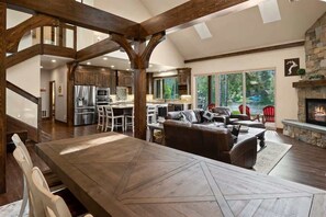 A spacious living area with a large wooden dining table, a fireplace, and a view of the outdoors.