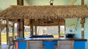 Eine Tiki-Bar mit einem Reetdach, einer Holztheke und zwei hölzernen Barhocker.
