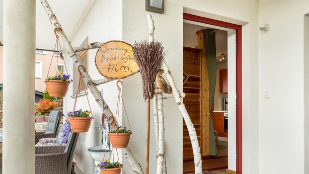 A hotel entrance with a wooden door, a sign with handwritten text, and potted plants.