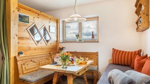 A cozy room with a wooden bench, a table with a vase of flowers, a sofa with cushions, and a window with a view of the sky.