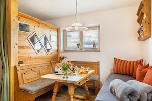 Et hyggeligt rum med en træbænk, et bord med en vase blomster, en sofa med puder og et vindue med udsigt til himlen.