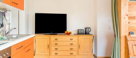 A kitchen with orange cabinets, a black TV, and a coffee maker.