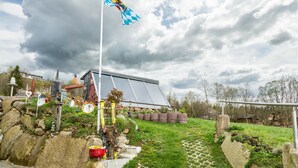 A house with a solar panel roof, a flagpole with a flag, and a garden with rocks and plants.