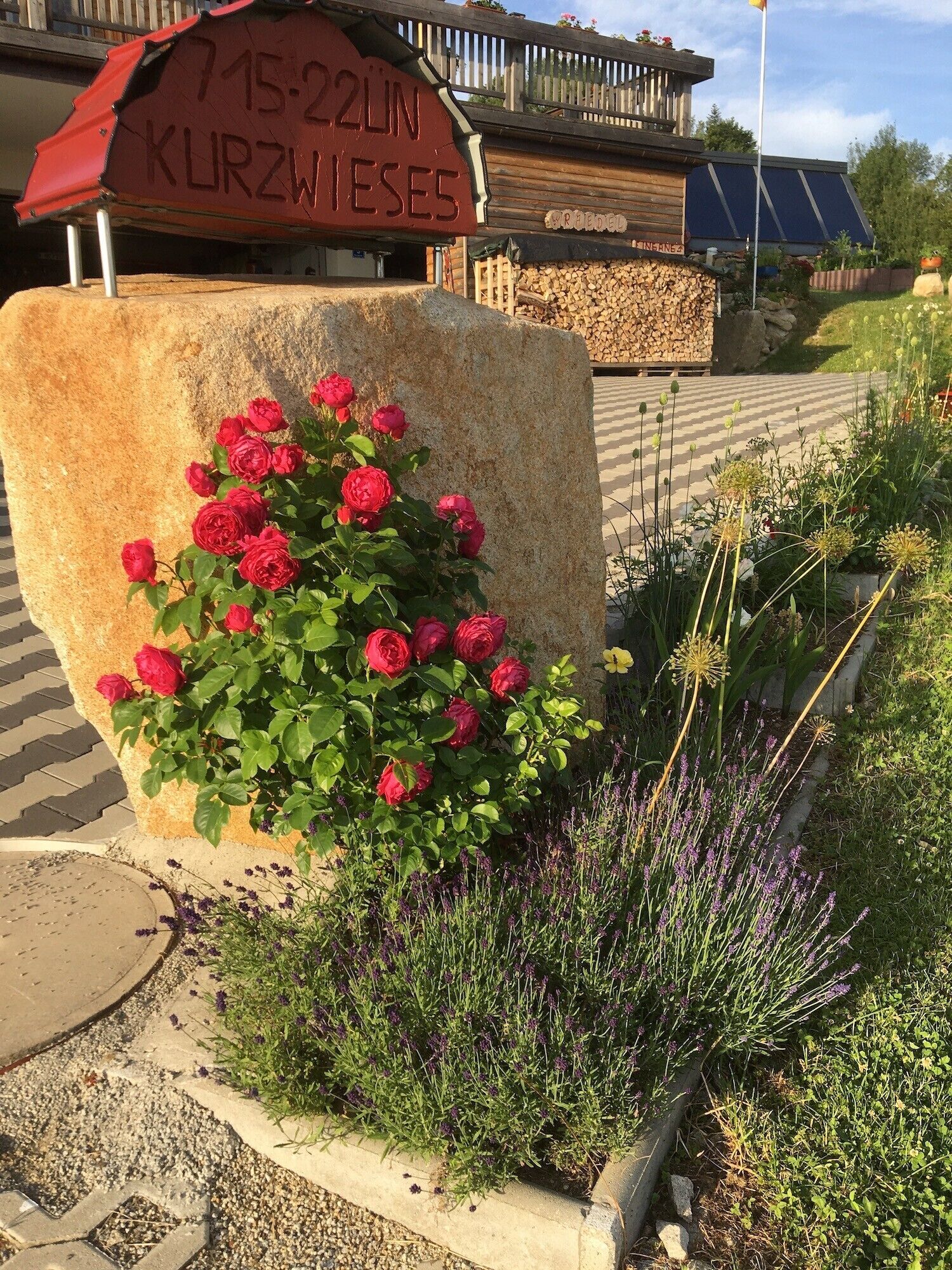 A stone sign with a date, a wooden building, and a garden with flowers.