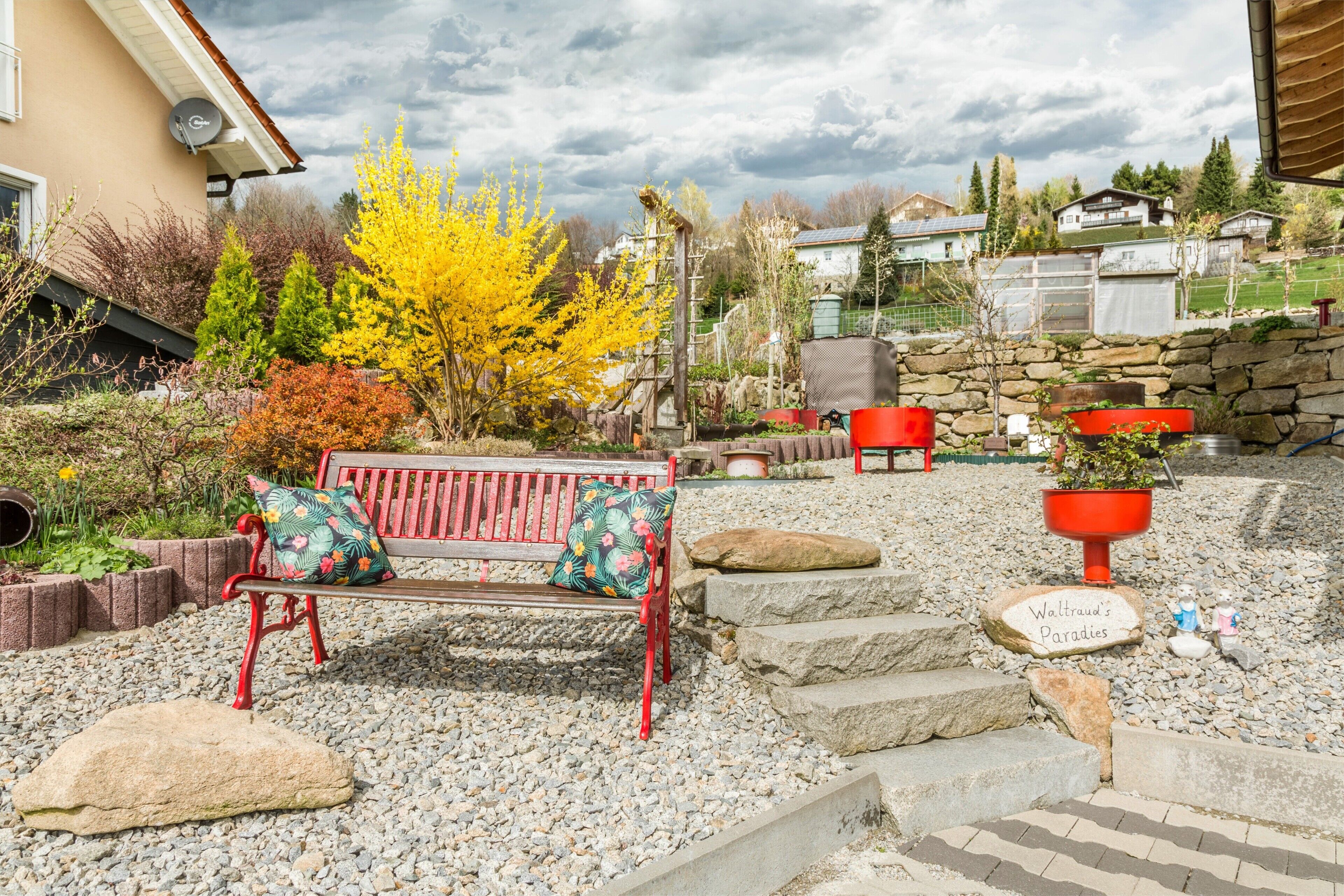 Ein Garten mit einer Bank, roten Pflanzkästen und einer Steinmauer.