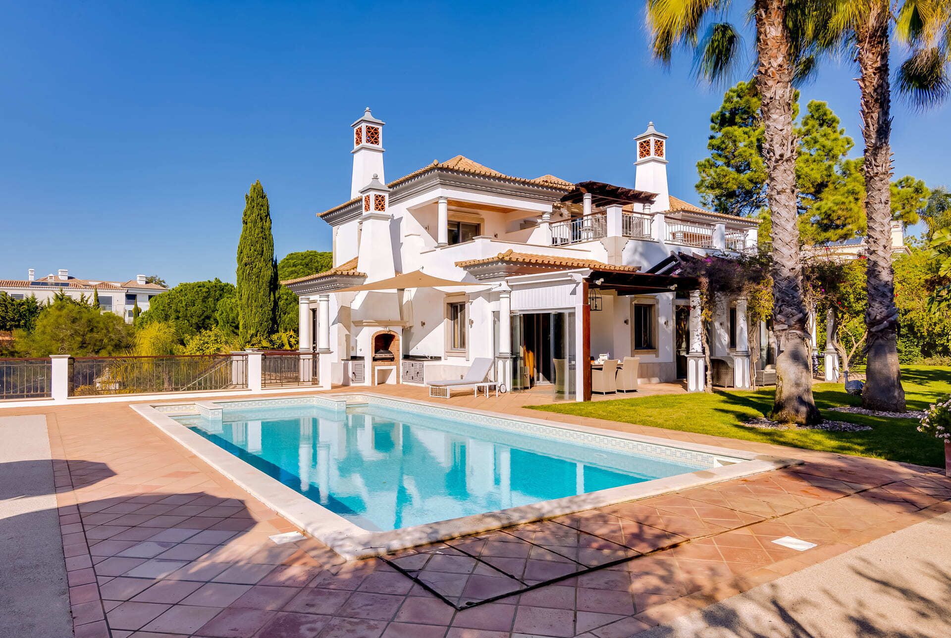 A large, white villa with a swimming pool, a patio, and a well-maintained garden.