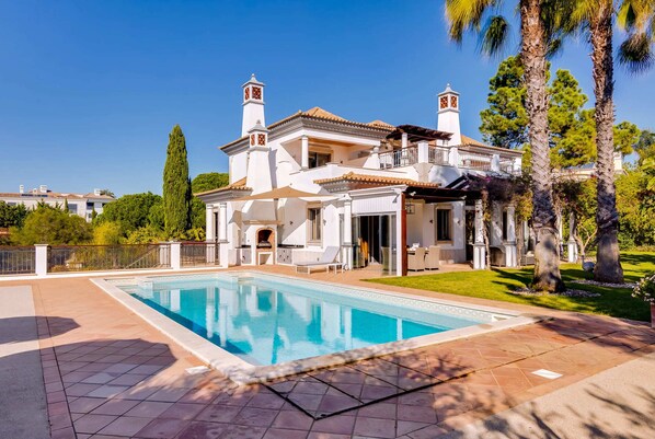 A large, white villa with a swimming pool, a patio, and a well-maintained garden.
