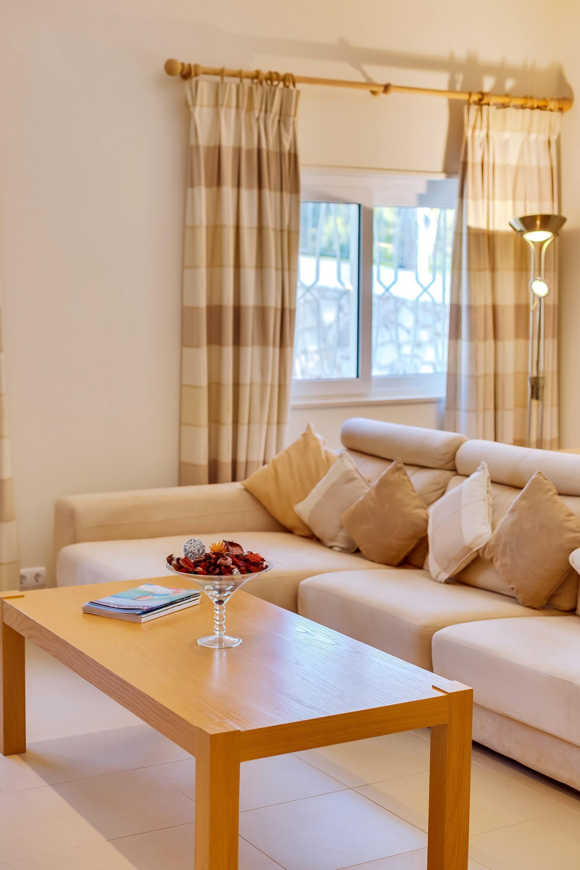 A living room with a beige sofa, a wooden coffee table, and a vase with flowers.