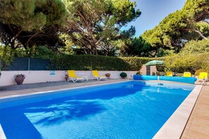 A swimming pool with clear blue water, surrounded by a tiled deck. There are several lounge chairs and a small umbrella providing shade. - 5 Star Villa Amari - Heatable Pool & Private Garden (Algarve)