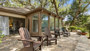 Une terrasse avec des fauteuils Adirondack, un espace clos par des parois de verre et un sol en briques.