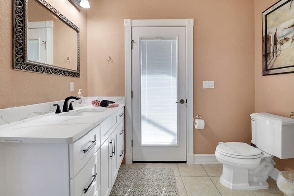 A bathroom with a white vanity, a toilet, and a door with a window.