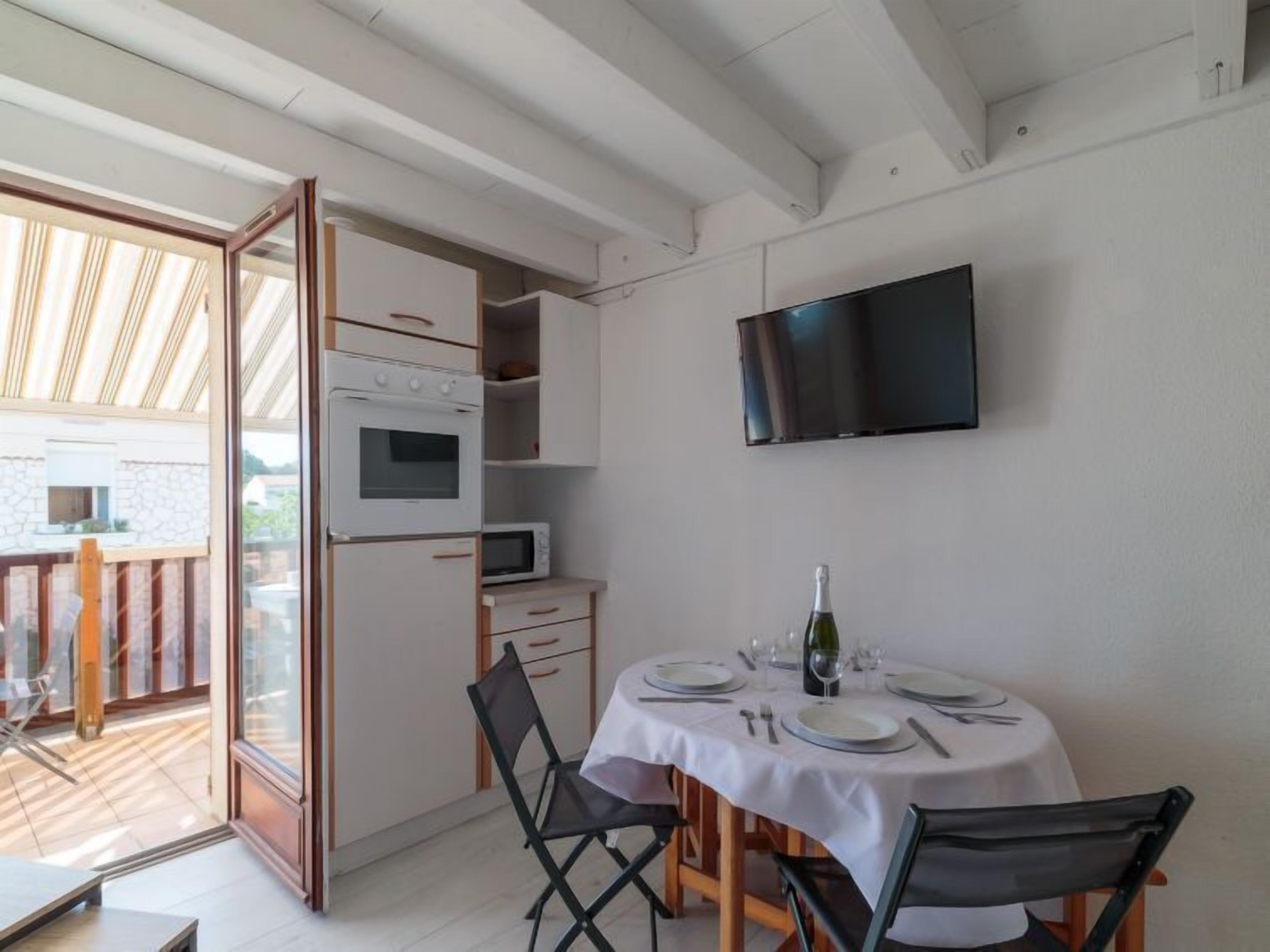 Ruokailutila, jossa on kahdelle katettu pöytä, seinälle asennettu televisio ja keittiö, jossa on kodinkoneet.