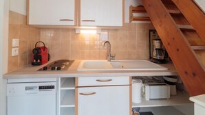 Eine kompakte Küche mit weißen Schränken, einem eingebauten Geschirrspüler und einer Holztreppe.