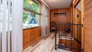 Un intérieur en bois avec une fenêtre donnant sur une maison bleue, une échelle en métal et un conteneur vert.