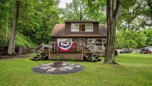 Une petite cabane avec une véranda, un drapeau et un foyer en pierre.