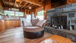 L’intérieur chaleureux d’un chalet avec un canapé rond en cuir, une cheminée en pierre, un plancher en bois et un coin cuisine.