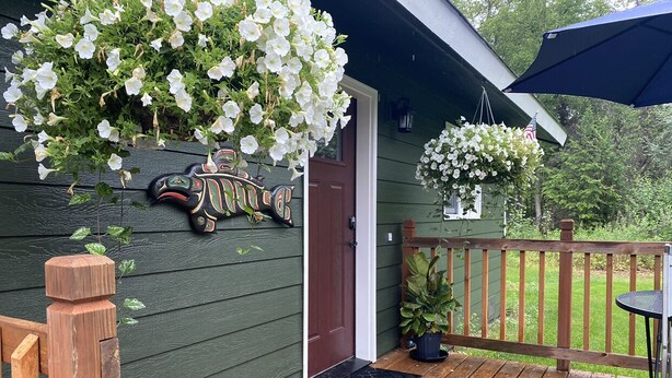 Une terrasse en bois avec une porte, une décoration représentant un oiseau suspendue et une plante en pot.